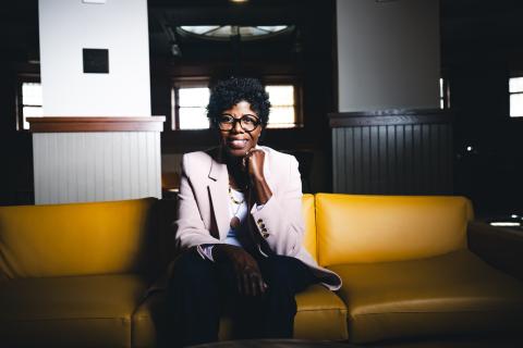 Robin Sundaramoorthy sits on a yellow sofa and smiles at the camera.